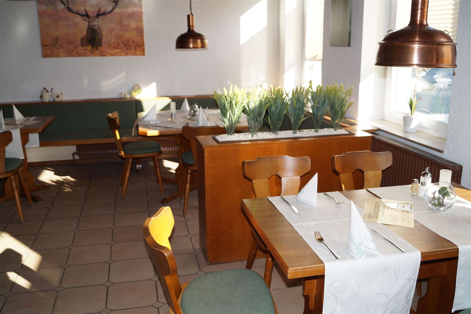Restaurant mit Holztischen, Kupferlampen und Hirschgemälde