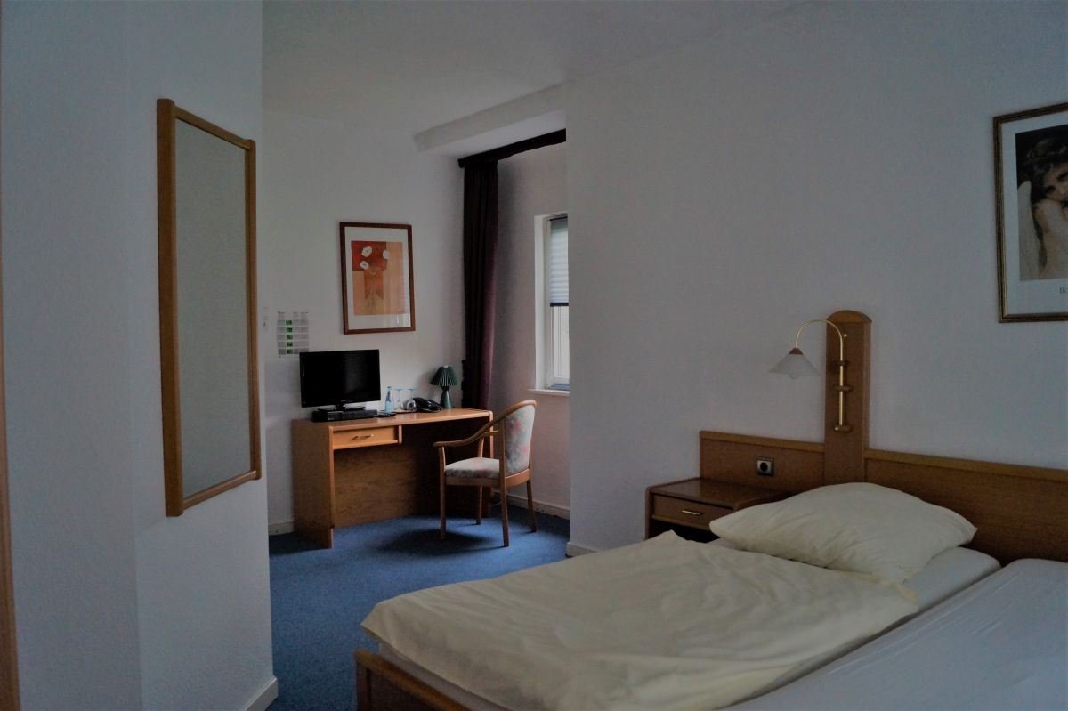 Gästezimmer mit Bett, Schreibtisch, Fernseher und Spiegel